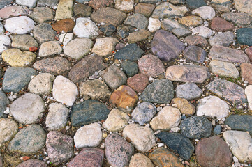 Cobblestone pavement. Background of cobblestones of different colors on the road. Ancient rough stones laid on the road.