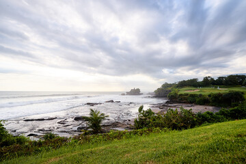 Beautiful balinese landscape. Ocean beach. Ancient hinduism temple Tanah lot on the rock against cloudy sky. Bali Island, Indonesia.