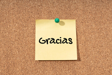 Thanks word in spanish language on yellow note on cork board