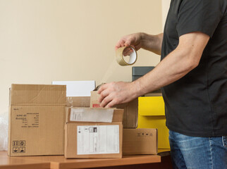 a man is taping a shipping box, a background table with shipping office boxes.