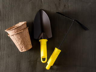 garden tools shovel and rake and peat cups on a dark background