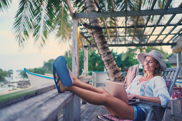 Technology and travel. Working outdoors. Freelance concept. Pretty young woman using laptop in cafe on tropical beach.