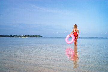 Enjoying suntan and vacation. Young woman in red swimsuit with pink rubber ring on the beach.