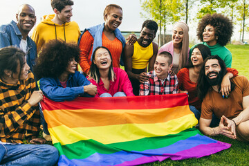 Diverse people having fun holding LGBT rainbow flag outdoor - Focus on center african woman face