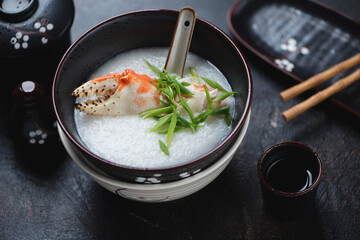 Bowl with crab congee or a type of asian rice porridge, studio shot on a dark-brown stone background