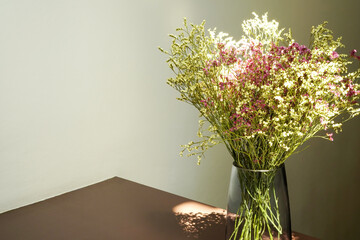 Dried pink and white Statice flower with glass vase under warm sunlight and shadow on beige background with copy space and selective focus