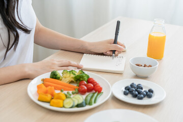 Obraz na płótnie Canvas Diet, Dieting hand of woman write diet plan right nutrition on table with fresh vegetables salad, almond is different food ingredients in the green. Nutritionist of healthy, nutrition of weight loss.