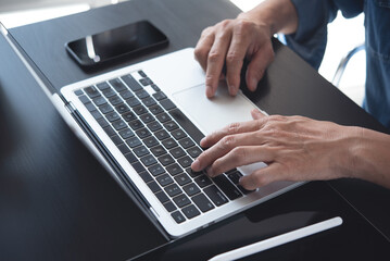 Closeup of a business man's hands working and typing on laptop computer keyboard on wooden table