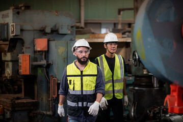 A latin mix race worker have unkempt beard and asian worker in safety uniform is working and control the heavy machine in industrial manufacturer factory.