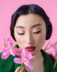 Close up portrait a beautiful young Chinese woman with black hair dressed in a green cloak on which are sewn fresh pink tulips