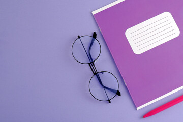 A purple school diary or a mock-up notebook, round glasses, a pen on a blue-purple background.The concept of teacher's day, things for businessmen, schoolchildren, education, planning.Copyspace