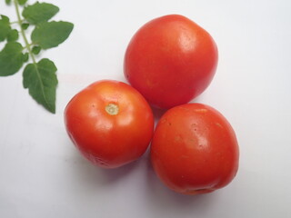 Three ripe red tomatoes and a tomato leaf on a white background