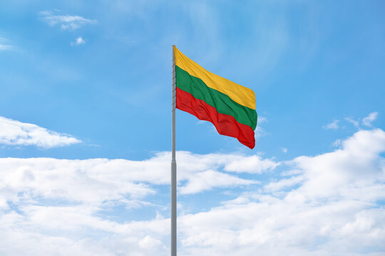 Flag of Lithuania is waving in front of blue sky and clouds