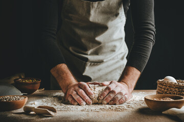 Young man kneading dough on dark background.