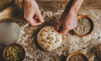 Young man kneading dough on dark background.