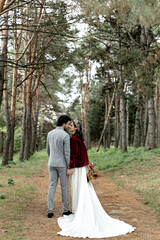 Beautiful young wedding couple hugging and walking in a pine forest