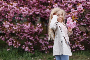 Beautiful girl with a branch of sakura in his hand on a background of blooming Japanese sakura tree