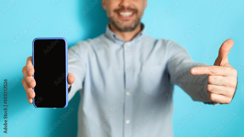 Poster man showing smartphone empty screen pointing finger, blue background, cropped