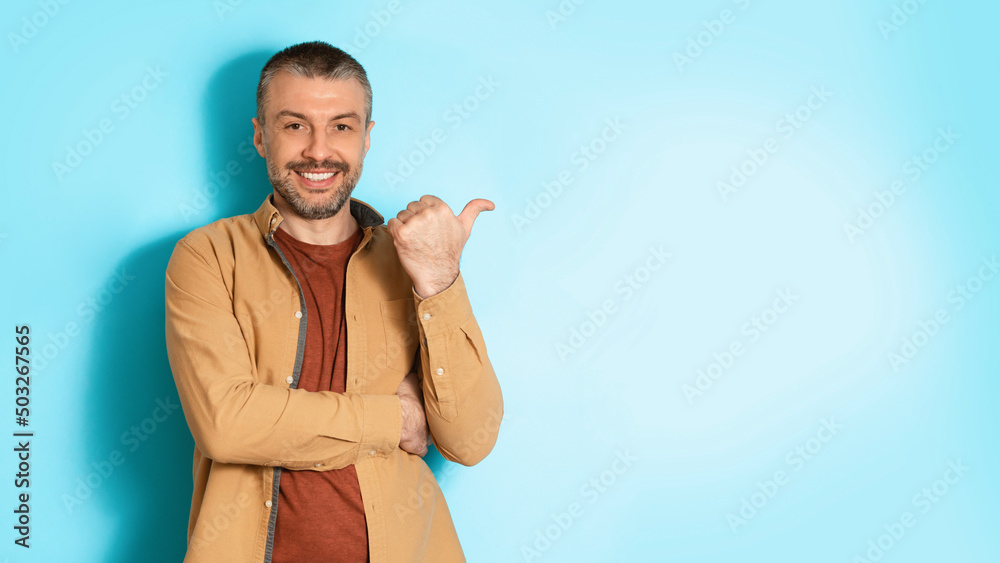 Poster man pointing thumb finger aside at copy space, blue background