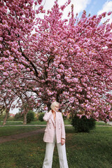 Stylish and beautiful woman in pink flowers on a spring day in the park near the blossoming sakura.