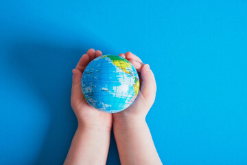 child's hands holding a ball in the form of a globe blue background
