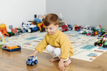 Little boy playing with cars in a bright children's room.
