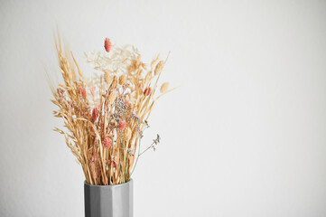 Beautiful dried flowers in a gray vase, against the background of a white wall in the interior. Wheat in a vase.