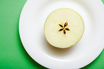 White plate with an apple half on green background.