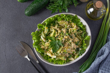 Salad with squid, cucumbers, boiled eggs and cheese in white bowl on green lettuce leaves