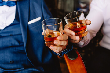 Two men holding a glass of whiskey in the groom's room. Cheers.