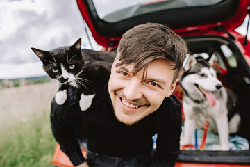 Husband cat on shoulders and husky dog in the background in the car.