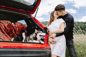 Travel concept with pets. A happy family is expecting a baby and resting with a cat and dog in nature near their car