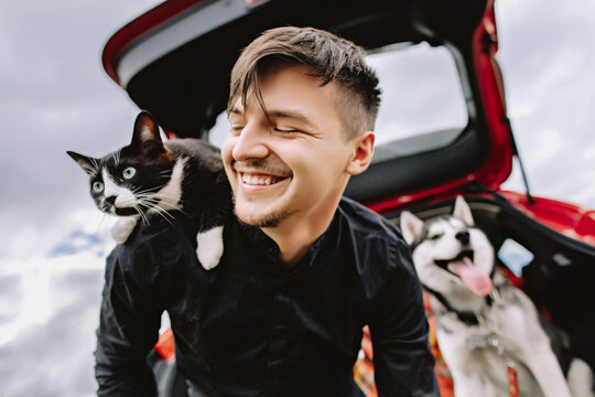Husband cat on shoulders and husky dog in the background in the car.
