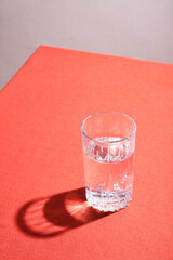 Glass of water with hard shadow on a table with red cloth.