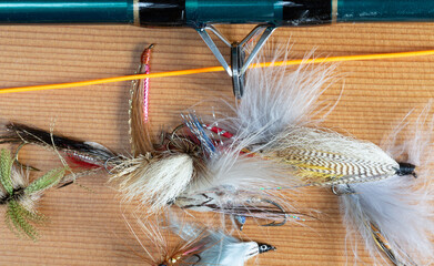 Close view of a fly rod with line and an assortment of flies for fly fishing on a wood background.
