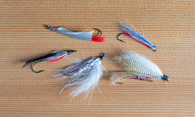 Five hand tied streamer fly fishing flies on a wood background.