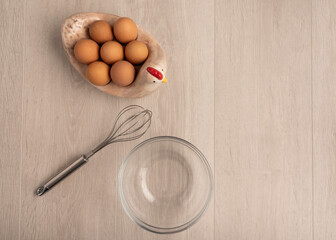 Eggs in a bowl and a whisk on a light wood background