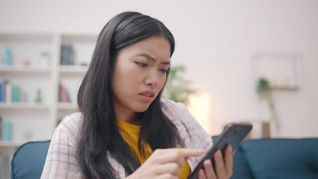 Young Asian woman reading bad news in social networks on phone, feeling upset