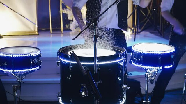 Three drummers perform a drum show in a club in front of an audience. Splashes fly from the blows on the drums