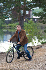 An adult blond man with a bicycle stopped by the river answer phone call.
