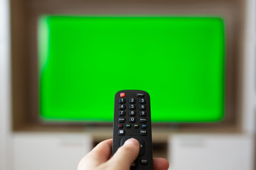 A hand with a TV remote control over a green screen. A place for your advertising