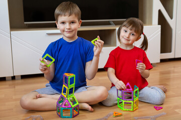 Brother and sister are playing with a magnetic construction toy. Magnetic constructor for the...