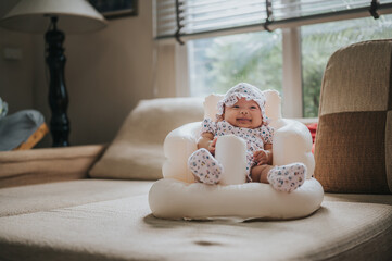 Fototapeta na wymiar Happy Asian baby girl sitting in Inflatable baby seat in living room
