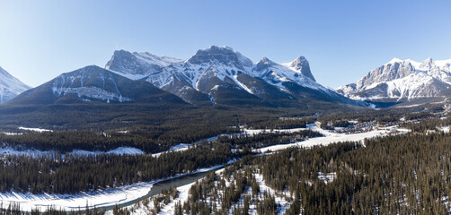Bow River valley forest in winter. Snowcapped Canadian Rockies beautiful scenery. Aerial panorama view. Three Sisters ridge and Mount Lawrence Grassi mountain range. Canmore, Alberta, Canada.
