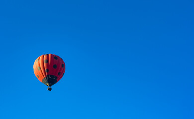 Red hot air balloon decorated as ladybird flying in clear blue sky