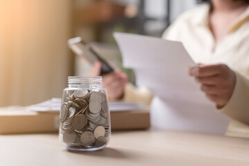 Woman pay the bills using mobile phone selective focus at tons of coin in a jar as concept of...