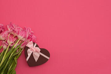 A beautiful composition of spring flowers and a gift box in the shape of a heart. Bouquet of pink tulips on a pink background. Valentine's Day, Birthday, Happy Women's Day, Mother's Day.