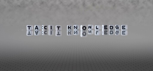 tacit knowledge word or concept represented by black and white letter cubes on a grey horizon background stretching to infinity - obrazy, fototapety, plakaty