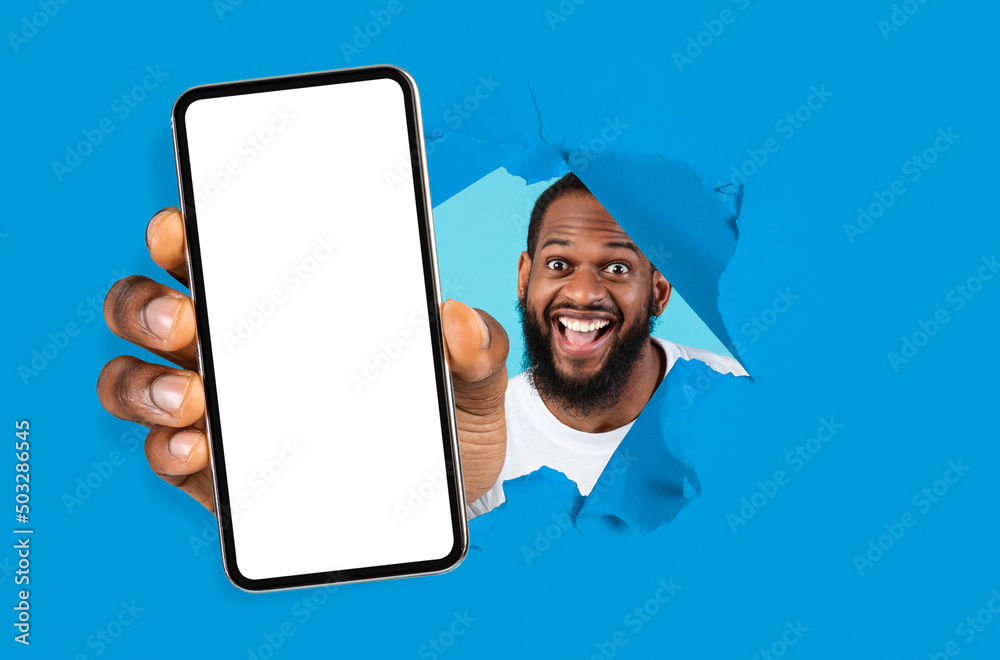 Poster excited guy showing white empty smartphone screen through torn paper