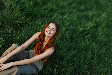 Naklejka na ściany i meble Happy woman smiling beautifully and looking up at the camera sitting on fresh green grass in the summer sunshine